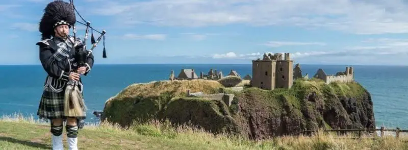 Vista del Castillo de Dunnottar junto a un escocés tocando la gaita