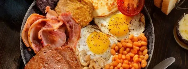 Desayuno típico escocés con haggis, huevos, pudding, salchichas, bacon, alubias, champiñones, tostada y tomates